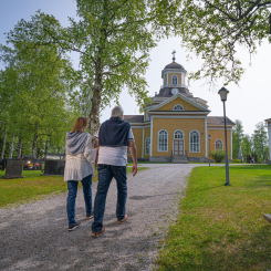 Kuvassa pariskunta astelee keväisenä päivänä kohti Kaustisen kirkkoa.