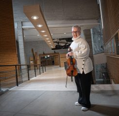 Sisäkuva Kansantaiteenkeskuksesta, jossa nainen  pitelee viulua ja hymyilee.