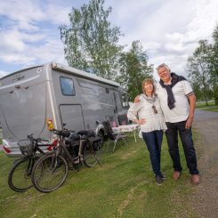 Vanhempi pariskunta hymyilee kameralle matkailuautonsa sekä pyöriensä vieressä.